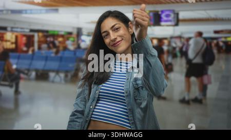 Die Frau gibt die Daumen nach unten, zeigt am Flughafenterminal einen Midriff, mit Blick auf die Kamera, Reisefrustration. Stockfoto