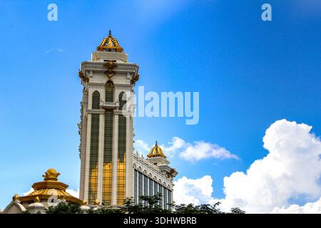 Flacher Blick auf einen luxuriösen weißen Turm mit goldenem Spiegelglas und kunstvollen goldenen Kuppeln unter einem hellblauen Himmel mit weißen Wolken. Stockfoto