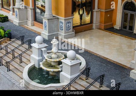 Klassischer, gestufter Wasserbrunnen aus weißem Stein in einem luxuriösen mediterranen Innenhof mit verzierten Säulen und schwarzen schmiedeeisernen Treppengeländern. Stockfoto