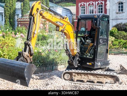 Pechory, Russland - 30. August 2024: Kleiner Baggerlader arbeitet am Bau einer neuen Straße am Sommertag. Сompact Baumaschinen für Arbeiten in Kalk Stockfoto