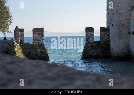 Blick auf die alten Steinmauern umschließen glitzerndes türkisfarbenes Wasser unter einem riesigen Himmel, eine zeitlose Szene, die an Geschichte und Gelassenheit erinnert, Sirmione, Lombardei, I Stockfoto