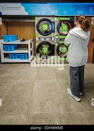 Eine Frau mit überkreuzten Armen wartet vor Trocknern in einem Waschsalon in Sevilla, Andalusien, Spanien. Sie wartet darauf, dass ihre Kleider fertig trocknen. Stockfoto