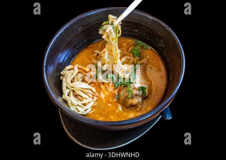 Northern Thai Khao Soi Hühnchen Curry Nudeln in schwarzer Schüssel auf schwarzem Hintergrund. Stockfoto