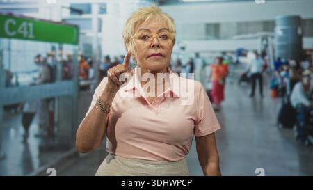 Frau zeigt mit dem Finger und dem Heck auf das Flughafenflugsteig c41, während sie Brille und rosa Polo trägt; Entscheidungsbefugnis. Stockfoto