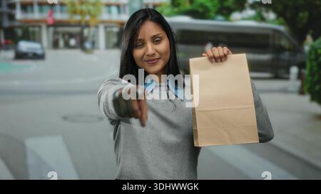 Frau, die auf der Straße steht, Tasche hält, lächelnd, stadtlänglich, Straße, Frau, lächelnd, braun, Tasche, Stadt, jung, zeigend, weiblich Stockfoto