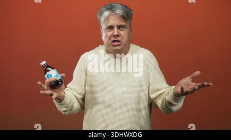 Mann mittleren Alters, der eine Arzneiflasche mit beiden Händen hält, mit offenen Händen zuckte Geste und sichtbare Handflächen in Richtung Kamera im Studio; Zweifel an Skepsis. Stockfoto