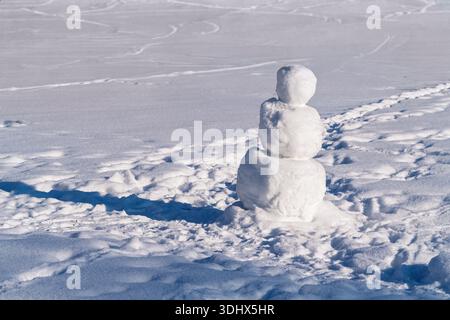 Da steht ein einsamer Schneemann auf einem verschneiten Feld, mit sichtbaren Fußspuren um ihn herum. Stockfoto