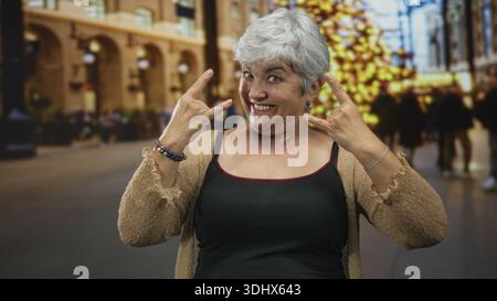 Frau Senior mit Tanktop und Strickjacke, die Steinhandgeste mit Händen und Lächeln im Bauen zeigt; spielerisches Selbstvertrauen. Stockfoto