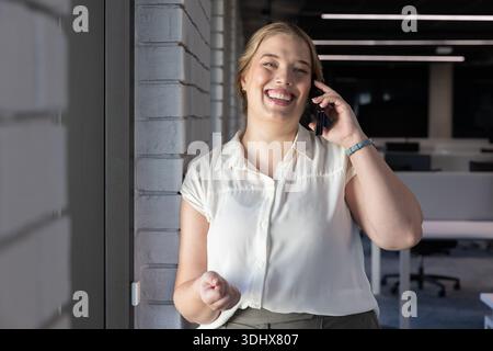 Weibliche Arbeiterin in weißer Bluse im Büro an der Ziegelsäule neben dem Fenster, telefoniert, gestickt Stockfoto