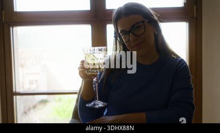 Frau genießt Wermut in einem mediterranen Restaurant, hält ein dekoratives Glas drinnen, zeigt eine junge hispanische schöne Szene mit einer entspannten Stockfoto