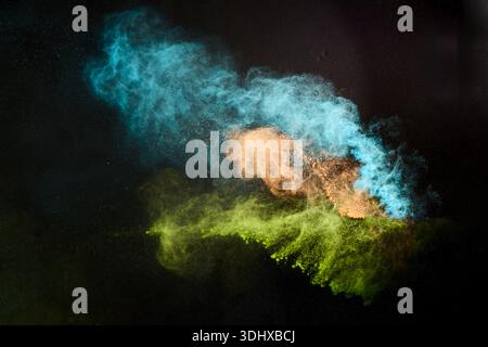 Buntes Pulver explodiert und schafft abstrakte, grüne türkisfarbene orangefarbene Formen Stockfoto