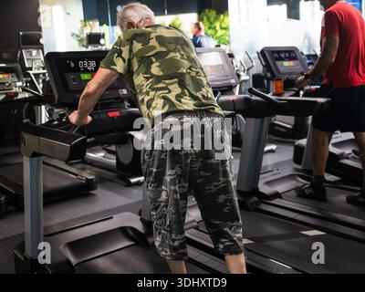 Ein älterer Mann in Tarnkleidung läuft auf einem Laufband in einem Fitnessstudio Stockfoto