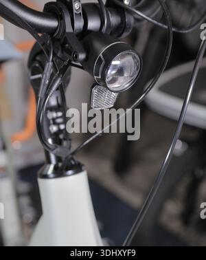 Nahaufnahme einer am Lenker montierten Frontleuchte für das Elektrofahrrad mit Reflektor, Montagehalterung und Seilzügen. Details zur Beleuchtung Stockfoto