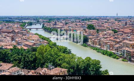 Weite Aussicht Auf Den Fluss Verona, Terrakotta-Dächer, Die Sich In Richtung Entfernter Kathedralentürme Erstrecken, Üppige Bäume Am Flussufer, Sonnige Sommeratmosphäre Stockfoto