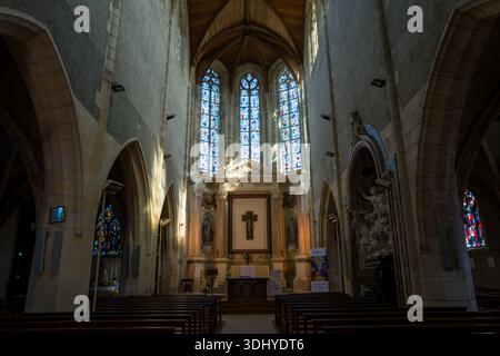 Unbekannter Ort - 13. April 2024: Das Bild zeigt das Innere einer historischen Kirche mit Holzbänken, einem Mittelschiff, einem großen Altar mit Kreuz, hohen Buntglasfenstern, gewölbter Decke und Steinbögen. Stockfoto