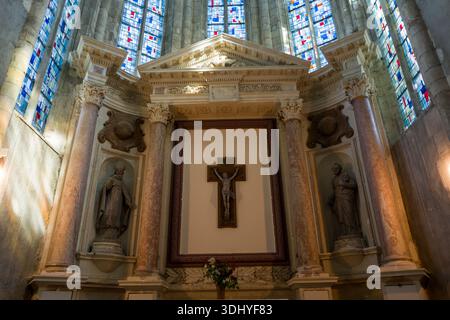 Unbekannter Ort - 13. April 2024: Das Bild zeigt den Hauptaltar einer Kirche mit einem zentralen Kruzifix, zwei Heiligenstatuen in Nischen, Marmorsäulen und darüber liegenden Buntglasfenstern. Stockfoto