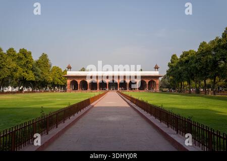 Delhi, Indien - 29. März 2024: Das Bild zeigt die Diwan-i-am, oder Hall of Public Audience, im Red Fort in Delhi, mit ihren roten Sandsteinbögen und dem weißen Dach, umgeben von grünen Rasenflächen und Bäumen unter klarem Himmel. Stockfoto