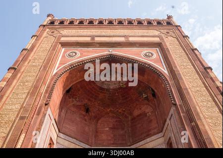 Fatehpur Sikri, Indien - 12. März 2024: Das Bild zeigt eine Nahaufnahme des Buland Darwaza, des monumentalen Haupteingangs zur Jama-Masjid-Moschee in Fatehpur Sikri, wobei der rote Sandsteinbogen, die komplizierten Schnitzereien und die arabischen Inschriften unter einem teilweise bewölkten Himmel hervorgehoben werden. Stockfoto