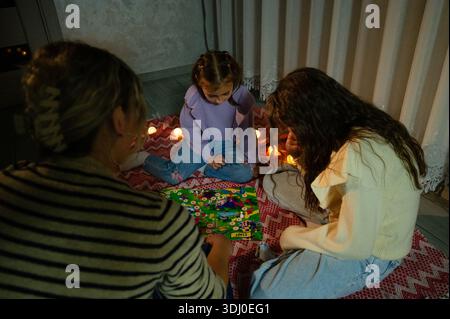 Eine Mutter und ihre beiden Töchter genießen einen Abend voller Verbundenheit und spielen ein lebhaftes Brettspiel, umgeben von warmem Kerzenlicht, das Freude und gemeinsam fördert Stockfoto