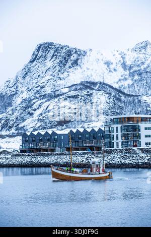 Svolvear, Lofoten Island, Norwegen Boot segelt im Wasser in der Nähe eines Berges. Das Boot ist klein und weiß. Das Wasser ist ruhig und der Himmel ist bewölkt. T Stockfoto