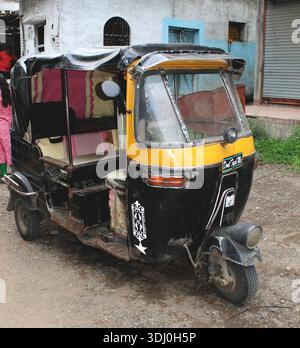 Traditionelle indische Auto-Rikscha, die auf einer Dorfstraße geparkt ist und alltägliche ländliche Transportmittel, verwitterte Texturen und das lokale Leben in Indien zeigt. Stockfoto