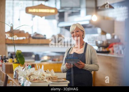 Porträt, Lächeln und Tablet mit alter Frau in Bäckerei für kleine Unternehmen oder Startup-Management. App, Schürze und Checkliste mit glücklicher Seniorin Stockfoto