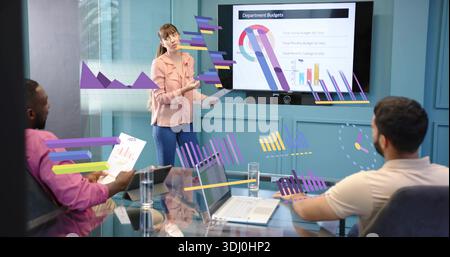 Eine Frau mit pfirsichfarbenem Oberteil, die im Besprechungsraum auf den Monitor zugeht, mit Budgetdiagrammen Stockfoto