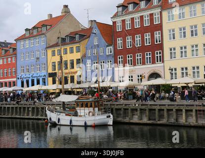 Kopenhagen, Dänemark-19. September 2025: Unbekannte Menschen sitzen und genießen den sonnigen Tag an den farbenfrohen Gebäuden mit Restaurants und verankertem Boot Stockfoto