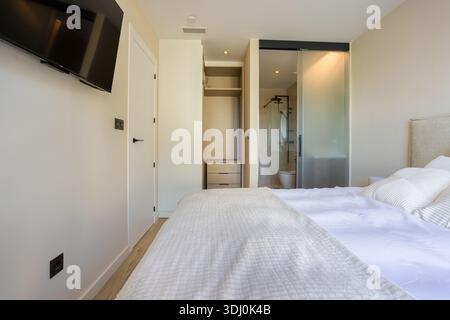 Minimalistisches Schlafzimmer mit Fernseher, Glasschiebetür im Badezimmer und hellem Holzfußboden Stockfoto