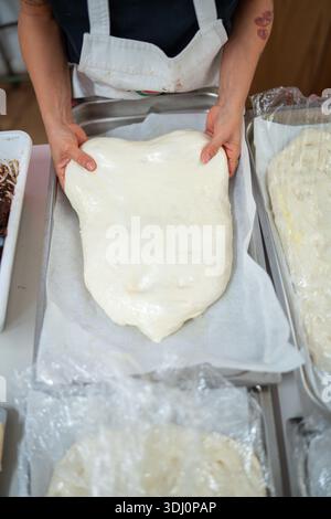 Die Hände einer Frau dehnen ein großes Stück frischer Nudelteig aus, der mit lokalen Zutaten gefüllt und zu Tortelli geformt werden kann Stockfoto