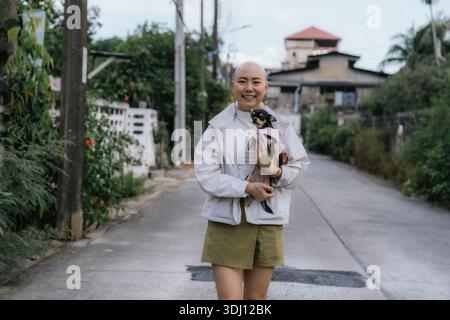Eine kahle Frau lächelt und hält chihuahua auf der Straße Stockfoto