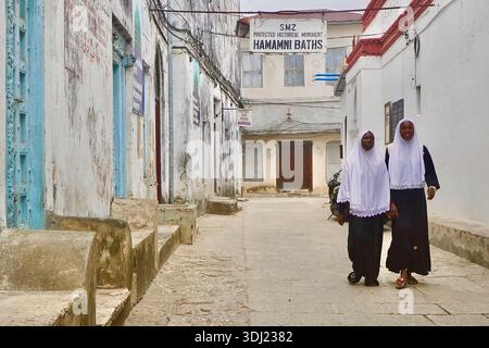 Zwei junge muslimische Frauen im traditionellen Hijab laufen in einer Gasse von Stone Town, Sansibar, Tansania Stockfoto