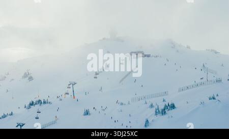 Die winterliche Szene mit teilweise nebelbedeckten Pisten der Skigebiete zeigt Skifahrer, Lifte und stimmungsvolle alpine Bedingungen Stockfoto