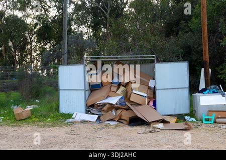 Überlaufender Metallbehälter, gefüllt mit gebrauchten Kartonschachteln am Rande eines Waldes. Das Konzept der Abfallentsorgung, Abfallentsorgung, Recycling und Umweltverschmutzung in der ländlichen Natur Stockfoto