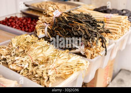 Auf einem Markt werden mehrere Körbe mit getrockneten Kräutern und Wurzeln gefüllt. In der Nähe gibt es auch Behälter mit getrockneten Früchten. Die Einstellung ist belegt und farbig Stockfoto