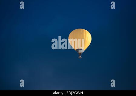 Ein gelber Heißluftballon mit Passagieren im Korb schwebt gegen einen tiefblauen Himmel. Stockfoto