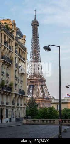 Der Eiffelturm erhebt sich über klassischen Pariser Wohngebäuden, von einer ruhigen Kopfsteinpflasterstraße in Paris, Frankreich, aus gesehen. Stockfoto