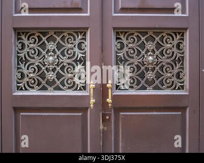Detaillierte Ansicht einer Vintage-Doppeltür mit komplizierten Metallgittern mit dekorativen Löwenköpfen und Messinggriffen Stockfoto