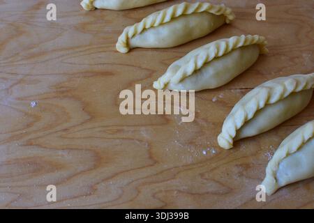 Traditionelles Kibinai-Gebäck von Karaim auf einem Holzbrett. Ungebackene Teigknödel mit verdrehten Kanten, beliebt in Trakai, Litauen, oft im Vergleich zu Kuchen Stockfoto