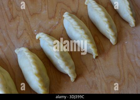Traditionelles Kibinai-Gebäck von Karaim auf einem Holzbrett. Ungebackene Teigknödel mit verdrehten Kanten, beliebt in Trakai, Litauen, oft im Vergleich zu Kuchen Stockfoto