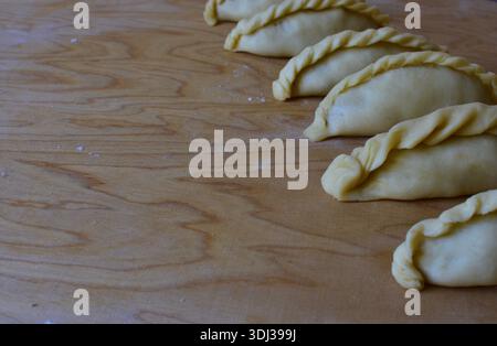 Traditionelles Kibinai-Gebäck von Karaim auf einem Holzbrett. Ungebackene Teigknödel mit verdrehten Kanten, beliebt in Trakai, Litauen, oft im Vergleich zu Kuchen Stockfoto