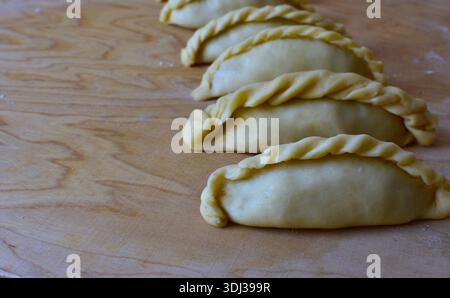 Traditionelles Kibinai-Gebäck von Karaim auf einem Holzbrett. Ungebackene Teigknödel mit verdrehten Kanten, beliebt in Trakai, Litauen, oft im Vergleich zu Kuchen Stockfoto