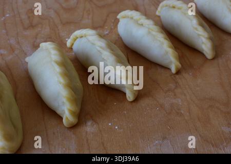 Traditionelles Kibinai-Gebäck von Karaim auf einem Holzbrett. Ungebackene Teigknödel mit verdrehten Kanten, beliebt in Trakai, Litauen, oft im Vergleich zu Kuchen Stockfoto