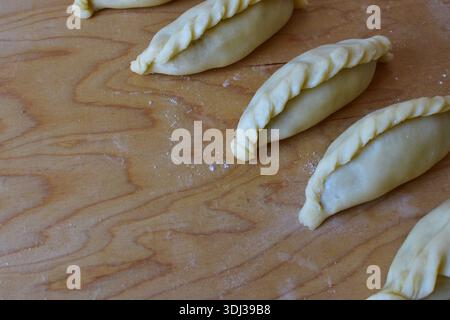 Traditionelles Kibinai-Gebäck von Karaim auf einem Holzbrett. Ungebackene Teigknödel mit verdrehten Kanten, beliebt in Trakai, Litauen, oft im Vergleich zu Kuchen Stockfoto