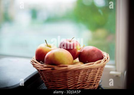 Frische Ernte von Äpfeln. Naturthema mit roten Trauben und Korb auf Fensterbank Hintergrund. Naturfrucht-Konzept. Stockfoto