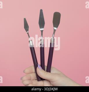 Die Hand hält 3-teilige Kuchencreme-Spatel auf rosafarbenem Hintergrund. Dekorationswerkzeugsatz Stockfoto