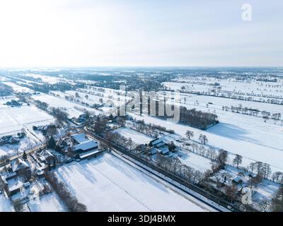 Blick aus der Vogelperspektive auf verschneite Ackerflächen mit blattlosen Bäumen, sich kreuzenden Straßen und fernen Horizont. Stockfoto