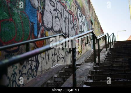 Städtische Betonmauer mit farbenfrohen Graffiti neben der Treppe. Metallgeländer und -Stufen im Winter, Street Art Kultur, düstere Stadtatmosphäre, pu Stockfoto