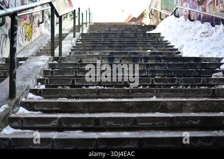 Betontreppen im Freien mit Eis und Schnee bedeckt, städtische Umgebung. Leere Treppe mit Metallgeländern, kaltes Wetter, städtische Infrastruktur Stockfoto