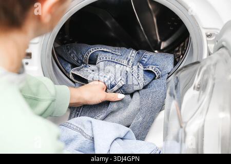 Blaue Jeans in moderner Waschmaschine waschen. Heimwäsche Routine-Nahaufnahme. Freizeitbekleidungspflege. Haushaltsreinigungskonzept. Stockfoto